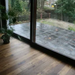 Dębowa podłoga w salonie z widokiem na taras po deszczu przez przesuwne okno balkonowe.