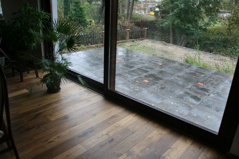 Dębowa podłoga w salonie z widokiem na taras po deszczu przez przesuwne okno balkonowe.