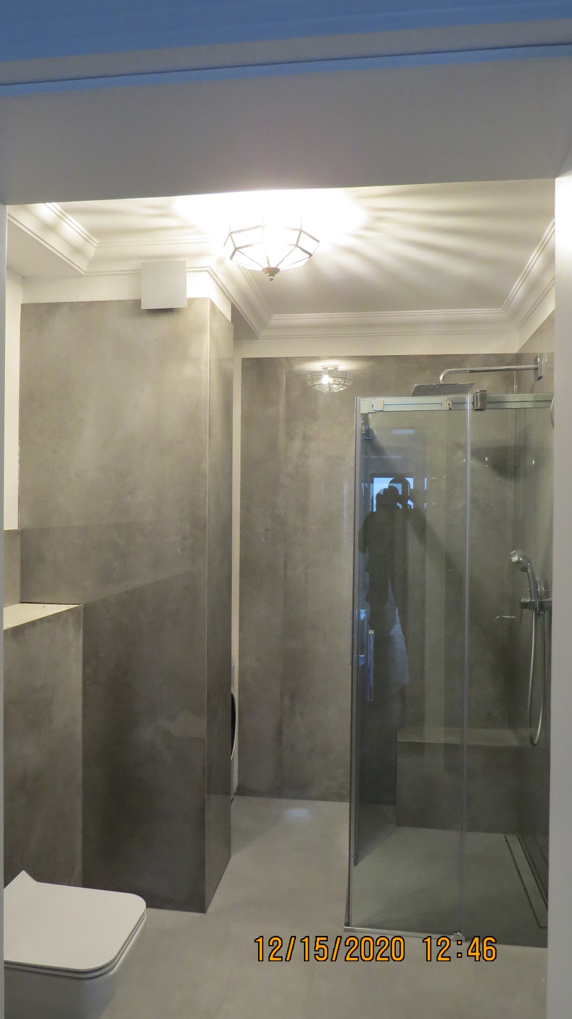 Nowoczesna łazienka z kabiną prysznicową typu walk-in, wykończona w szarym mikrocemencie, z podwieszaną toaletą i oświetleniem sufitowym.