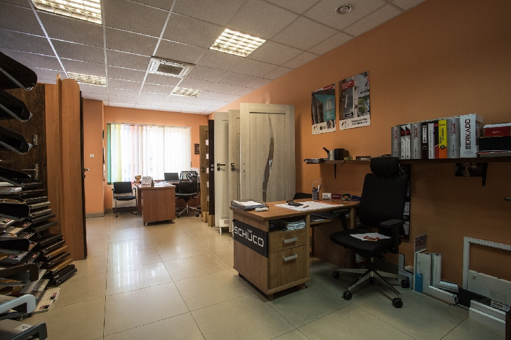 Wnętrze biura firmy Ryta&Syn z ekspozycją drzwi wewnętrznych, biurkami i krzesłami biurowymi oraz regałami z dokumentami i materiałami reklamowymi.