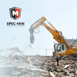 Żółta koparka z hydraulicznymi nożycami do betonu na gruzowisku po rozbiórce, w tle widoczne dźwigi, w lewym górnym rogu logo firmy SPEC-MIN.