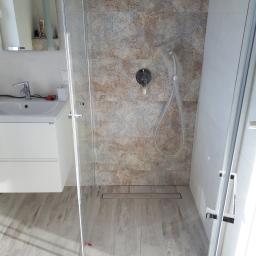 Kludi Uslugi remontowe i ogrodnicze - Nowoczesna łazienka z kabiną prysznicową typu walk-in, wykończona płytkami w odcieniach beżu i błękitu, z odpływem liniowym w podłodze imitującej drewno. Bateria prysznicowa z deszczownicą w folii...