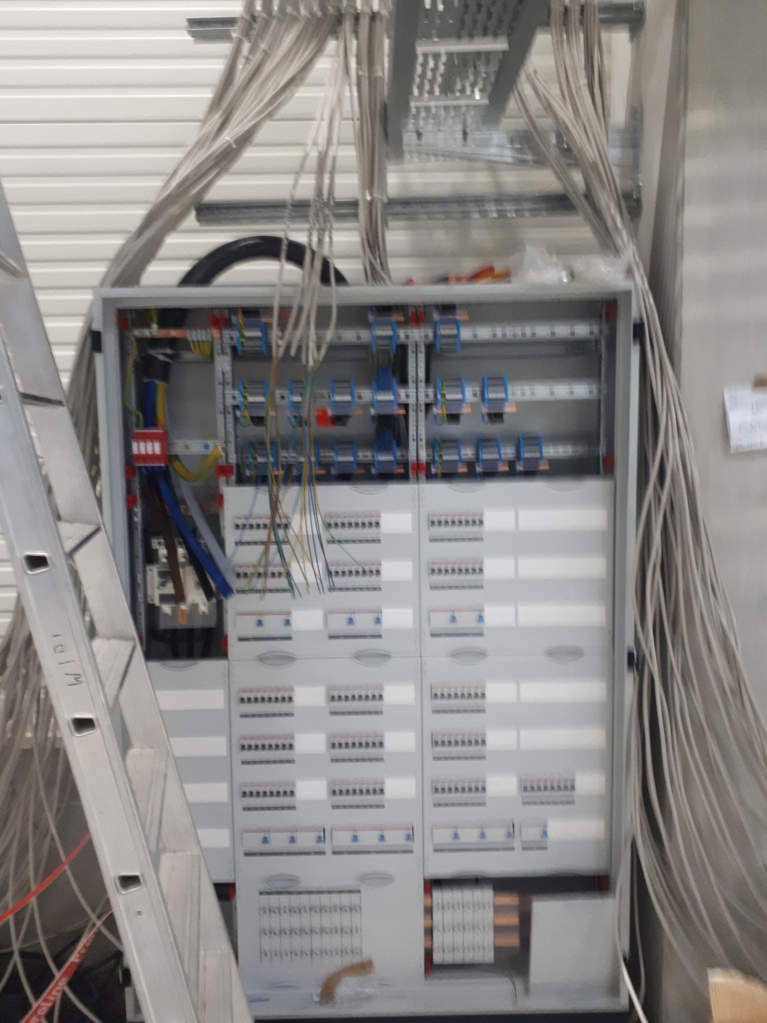 Szafa elektryczna z licznymi przewodami w trakcie montażu instalacji elektrycznej w Wałbrzychu, widoczna drabina oparta o szafę.