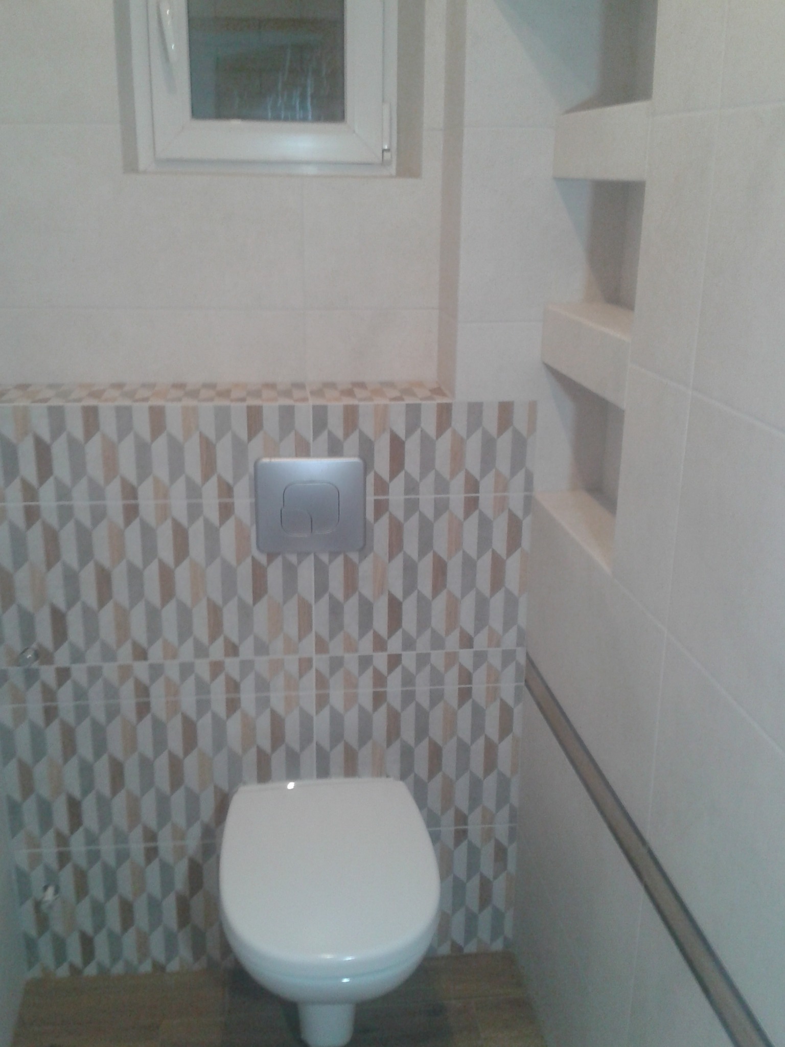 Wykończona toaleta z geometryczną mozaiką na ścianie, białą ceramiką i wnękami w ścianie.