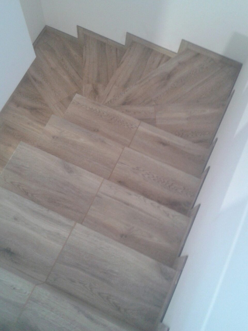 Schody wyłożone płytkami imitującymi drewno, widok z góry, jasne ściany.