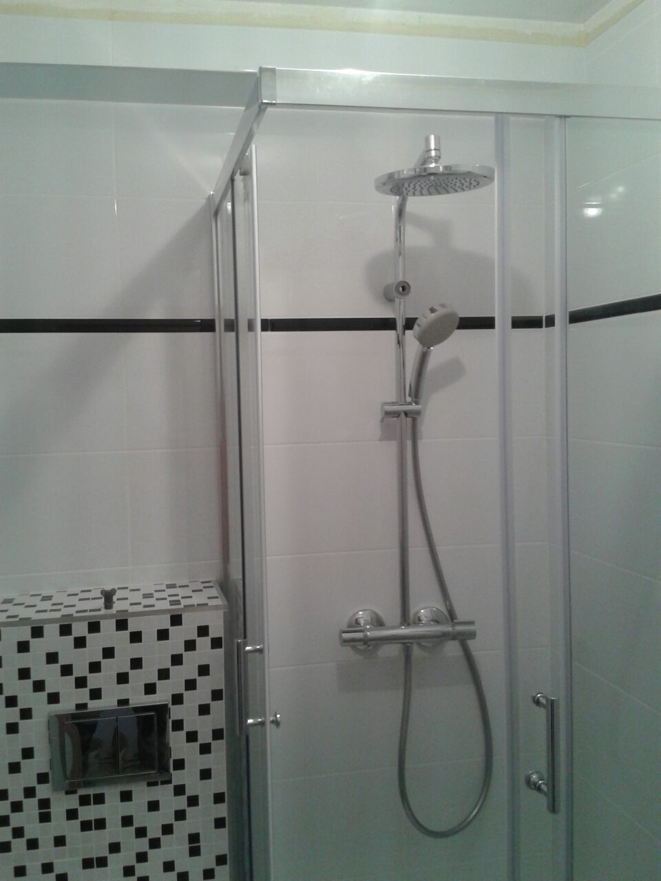 Nowoczesna kabina prysznicowa z deszczownicą, białe płytki z czarnym paskiem, zabudowa WC w czarno-białą mozaikę.