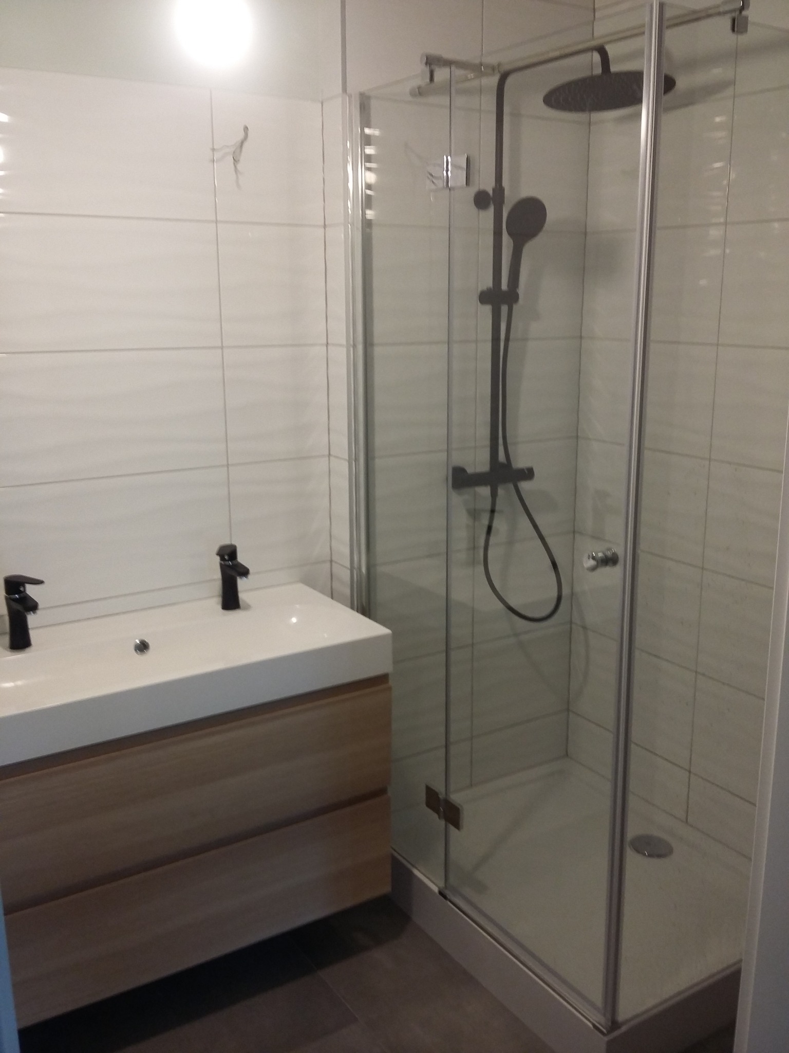 Nowoczesna łazienka z kabiną prysznicową typu walk-in z czarną armaturą i umywalką z szafką z jasnego drewna.