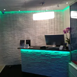 Recepcja z kamienną ścianą, podświetlona zielonymi ledami, wisząca lampa i monitor Lenovo.