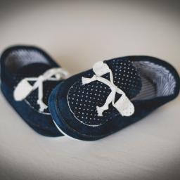 Fotografia i filmowanie Adam Sielski - Dwa granatowe, miękkie buciki niemowlęce z białymi sznurówkami i wzorem w białe kropki, ustawione obok siebie na jasnym tle.