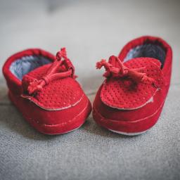 Fotografia i filmowanie Adam Sielski - Dwa czerwone, zamszowe buciki niemowlęce z dziurkowanym wzorem i sznurowadłami, leżące na szarym tle.