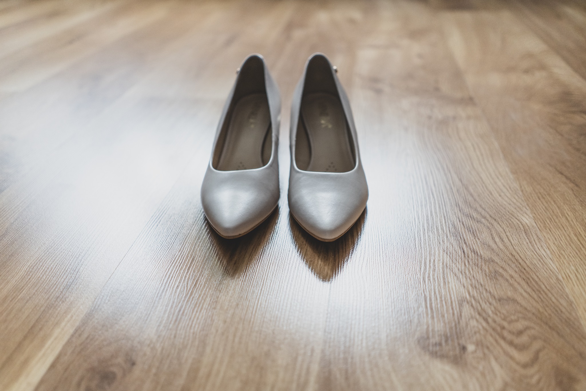 Para srebrnych, satynowych szpilek ślubnych ustawionych na drewnianej podłodze, widok z przodu.