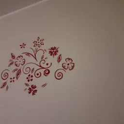 Biała ściana z dekoracyjnym, bordowym wzorem kwiatowym i roślinnym w lewym górnym rogu.