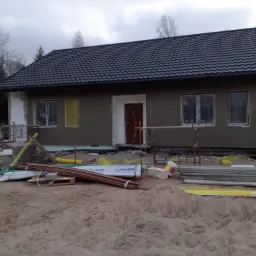 Dom jednorodzinny w Lubowidzu w trakcie prac związanych z wykończeniem elewacji, widoczne rusztowania i materiały budowlane.