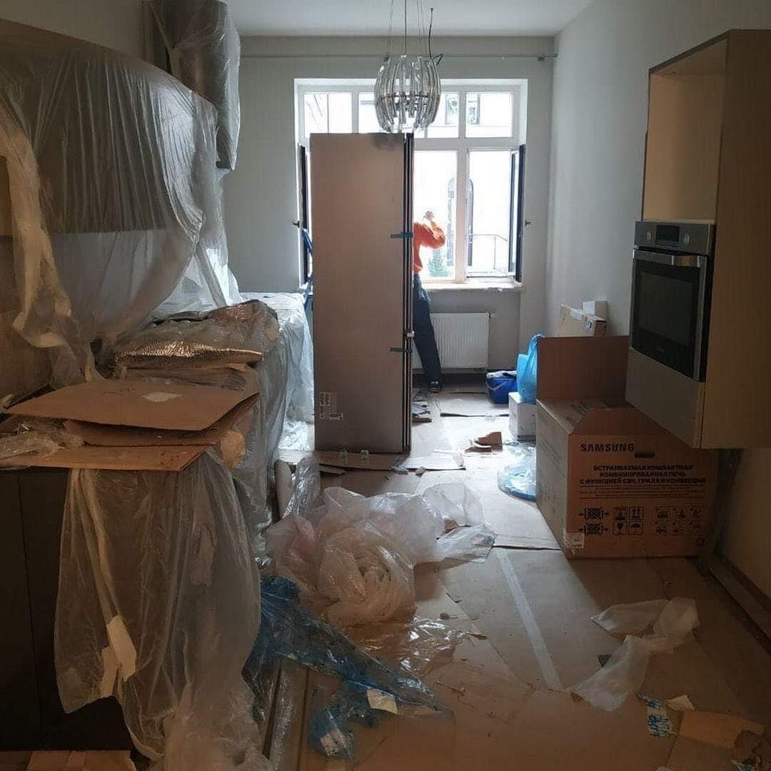 Kuchnia w trakcie montażu: meble częściowo zabezpieczone folią, kartony na podłodze, widoczny montażysta przy oknie.