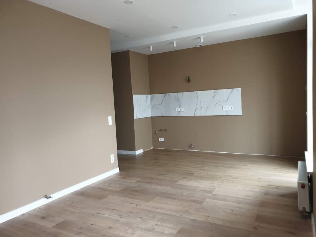 Pomalowane na beżowo wnętrze pokoju z panelami podłogowymi, białymi listwami przypodłogowymi i marmurowym panelem nad gniazdkami elektrycznymi.