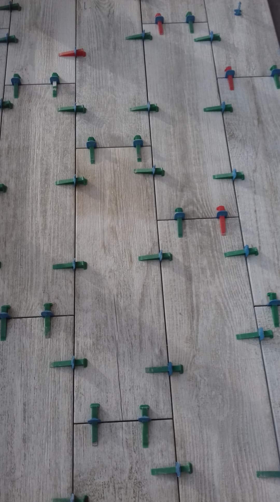 Ułożone płytki podłogowe imitujące drewno, z widocznymi, kolorowymi klinami dystansowymi, zapewniającymi równe odstępy między płytkami.