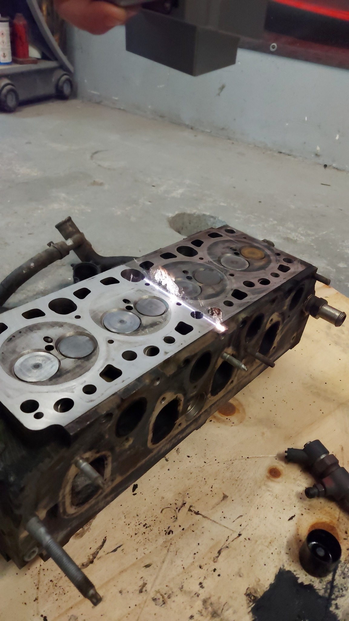 Czyszczenie głowicy silnika spalinowego za pomocą lasera. Widoczne iskry i dym podczas usuwania zabrudzeń z powierzchni metalu.