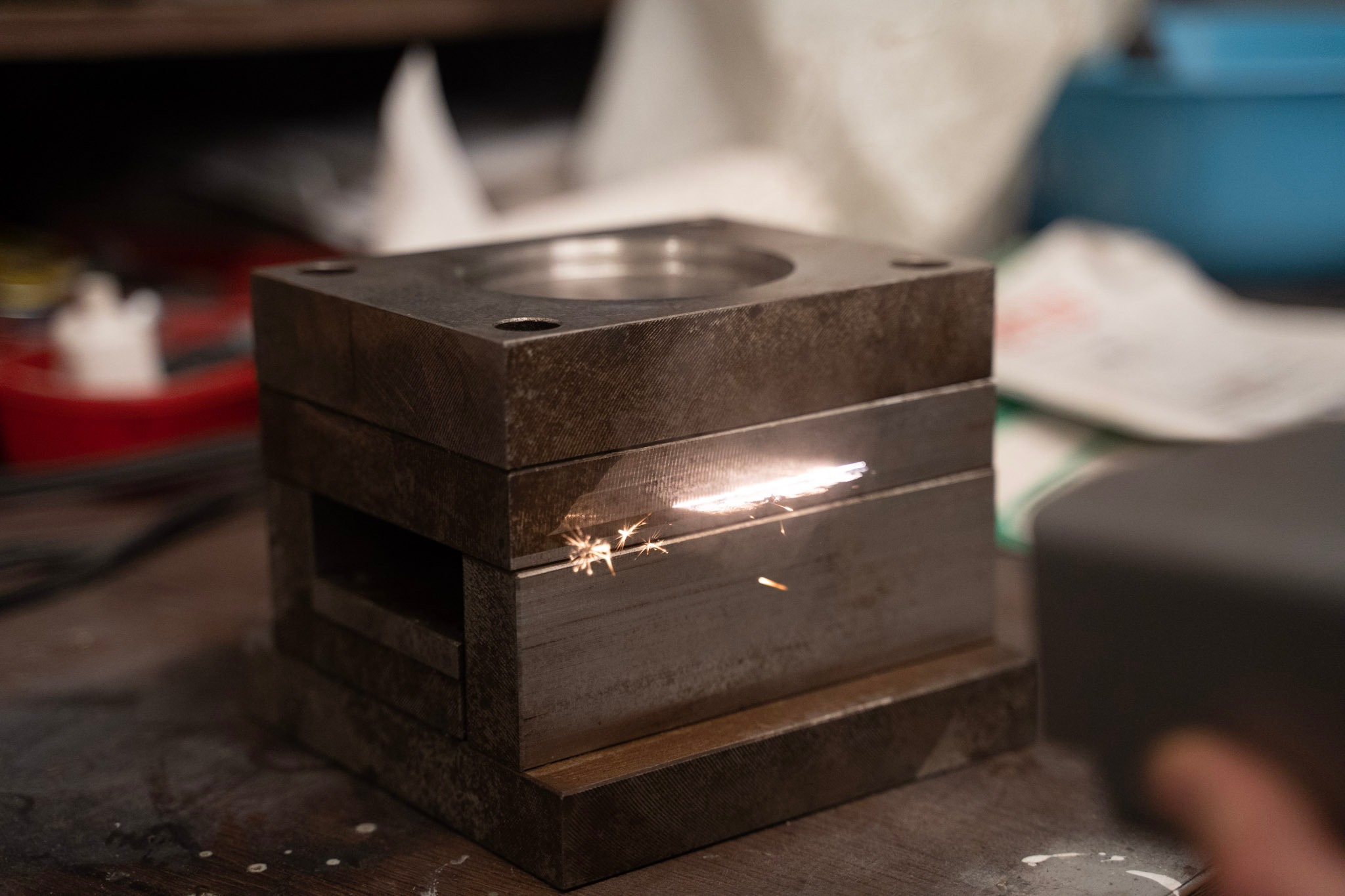 Metalowy blok z iskrzącą szczeliną, prawdopodobnie poddawany obróbce laserowej, widoczne wióry i iskry.