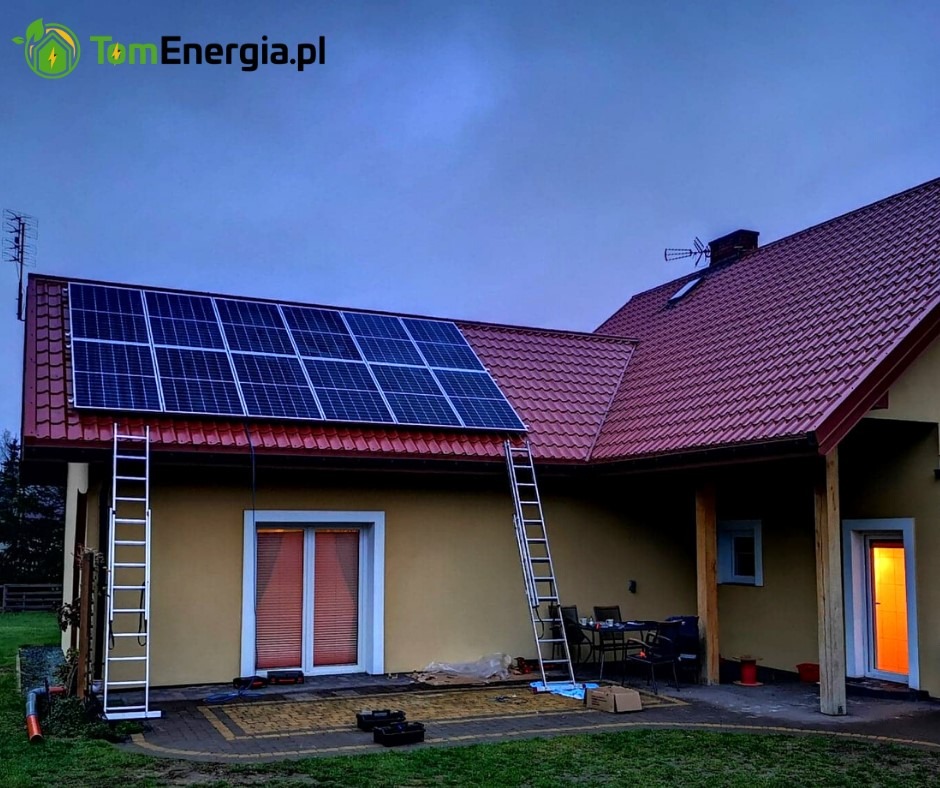 Montaż paneli słonecznych na dachu domu jednorodzinnego, widoczne dwie drabiny opierające się o dach, wieczorny krajobraz