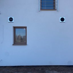 MarKal INSTAL - Elewacja budynku z zamontowanymi kratkami wentylacyjnymi, oknem z brązową ramą i wystającymi przewodami elektrycznymi