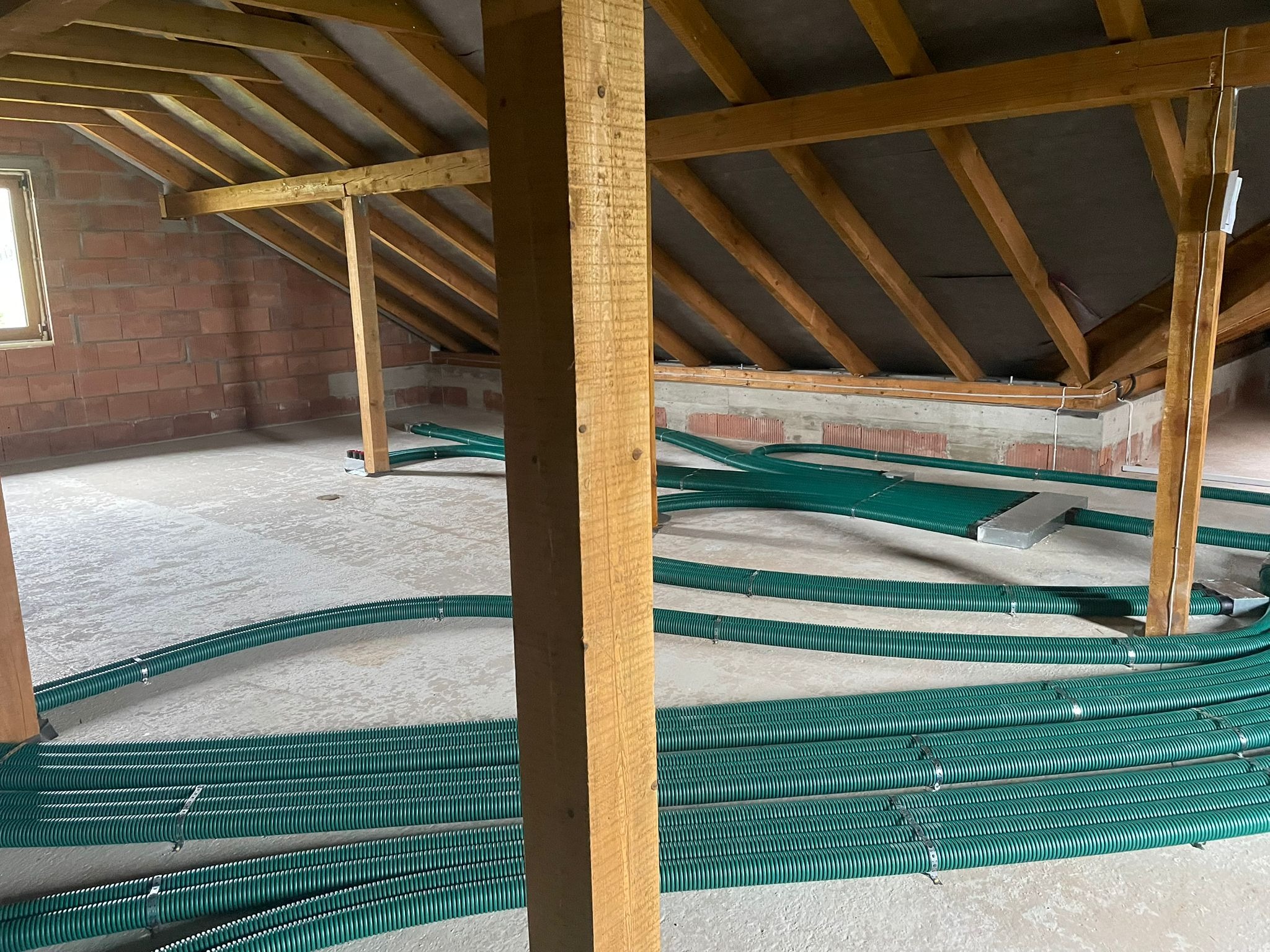 Poddasze z widoczną konstrukcją dachu i ułożonymi, zielonymi przewodami wentylacyjnymi. Widoczna instalacja przed zakryciem, surowy stan wykończenia.