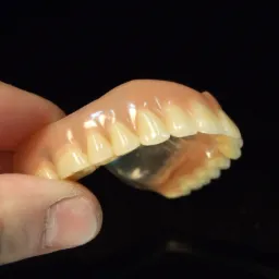 Częściowa proteza zębową w dłoni na czarnym tle, widoczna struktura akrylowej bazy i sztucznych zębów.