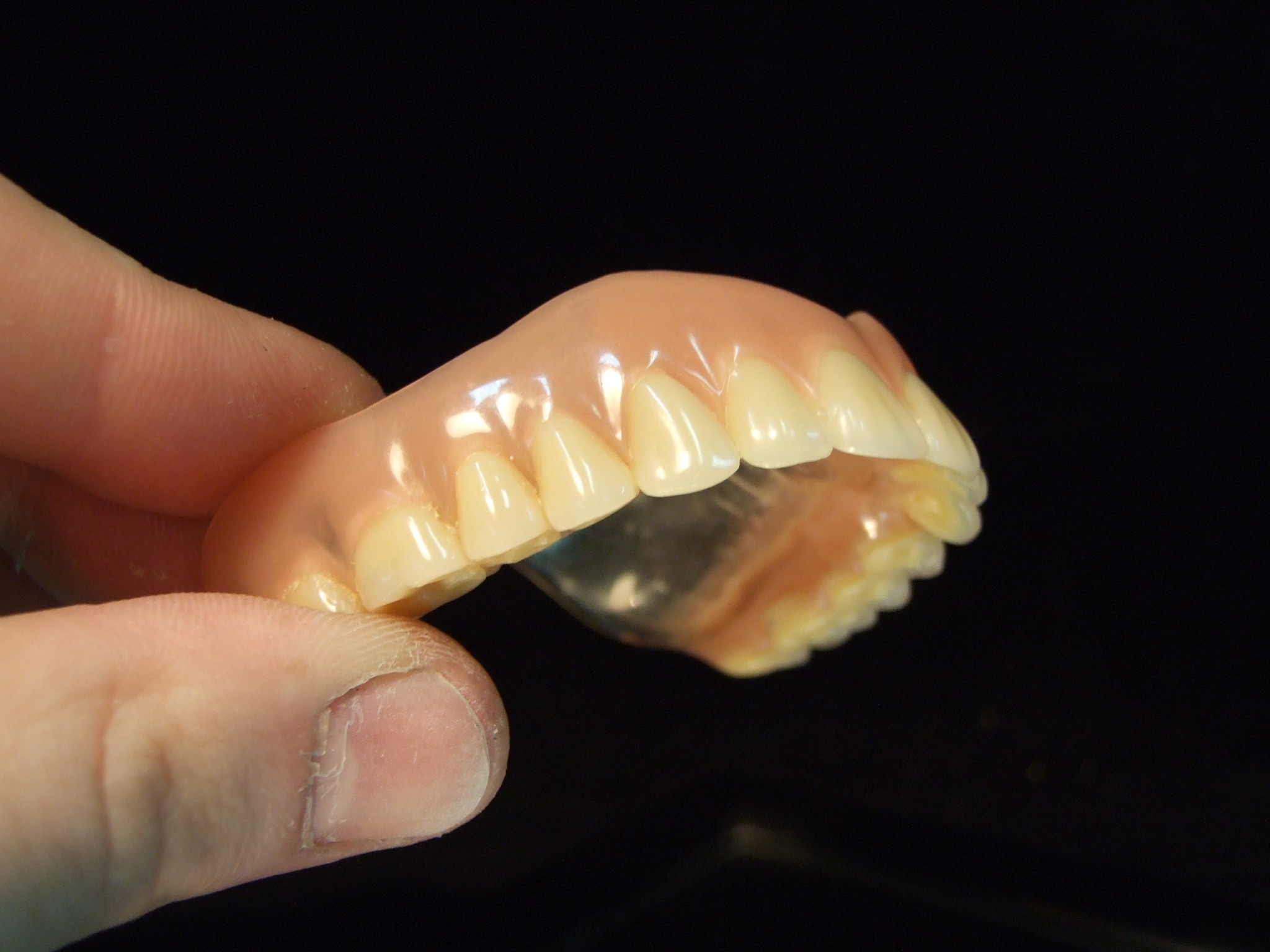 Częściowa proteza zębową w dłoni na czarnym tle, widoczna struktura akrylowej bazy i sztucznych zębów.