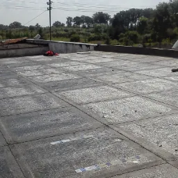 Betonowy taras z widocznymi podziałami na kwadratowe pola, częściowo pokryty resztkami po pracach budowlanych, z widocznymi elementami konstrukcyjnymi i narzędziami w tle.