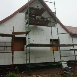 Ocieplanie budynku styropianem, widoczne rusztowanie i zaklejone okna płytami OSB.