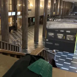 Toga adwokacka z zielonym żabotem leżąca na marmurowym parapecie w holu Sądu Okręgowego w Warszawie, widok z góry na kolumny i posadzkę.