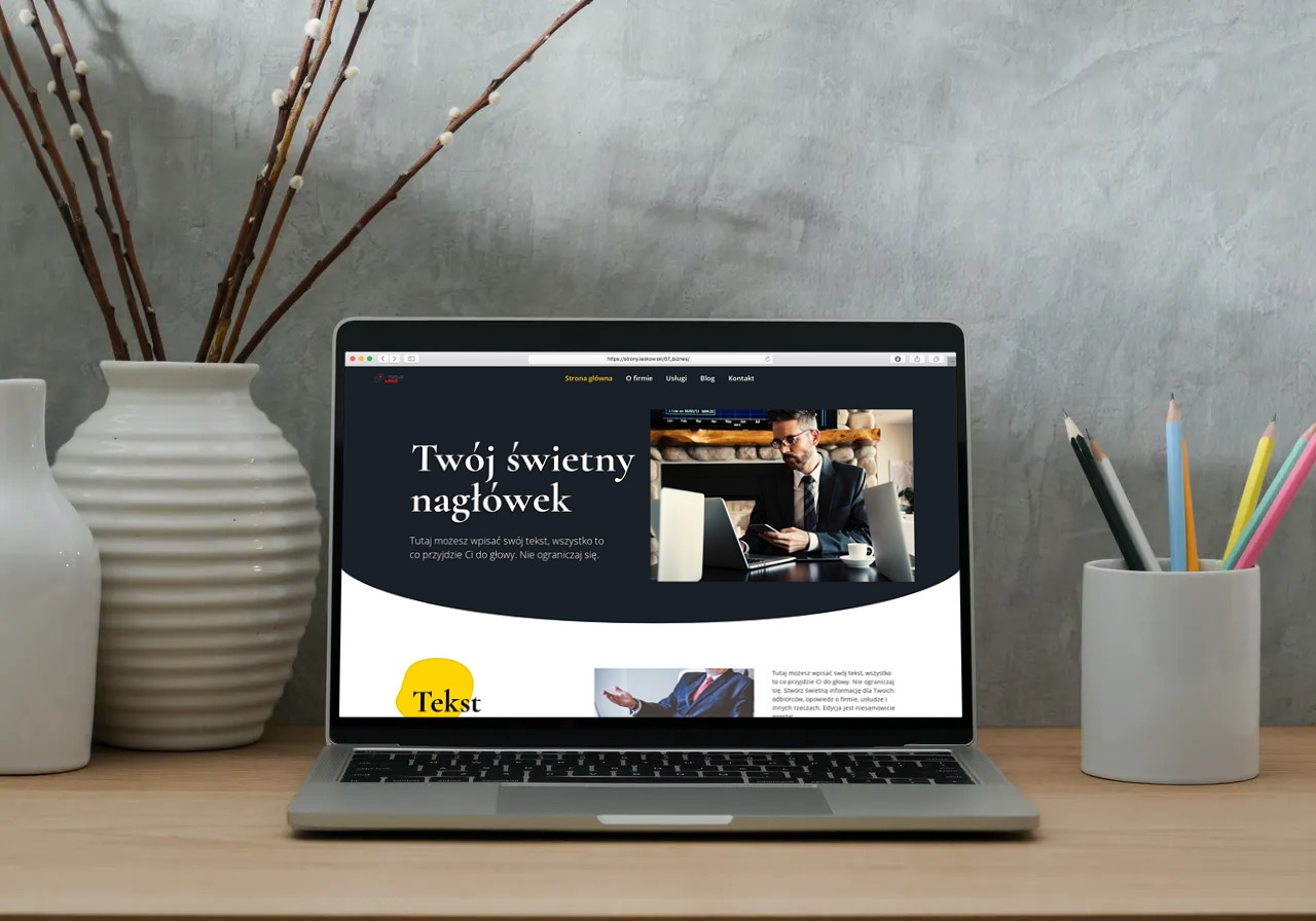 Laptop wyświetlający przykładową stronę internetową z nagłówkiem 'Twój świetny nagłówek', ustawiony na biurku obok wazonu z gałązkami i pojemnika z kredkami.