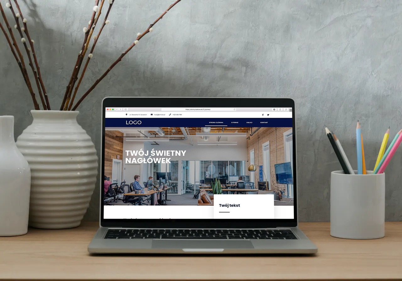 Laptop wyświetla projekt strony internetowej z nowoczesnym biurem w tle, obok wazon z gałązkami i pojemnik z kredkami.