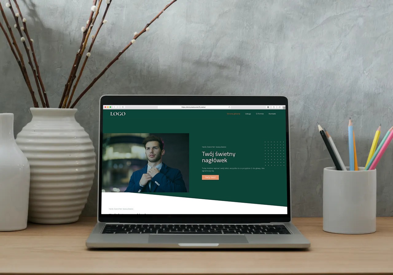 Laptop wyświetla zieloną stronę internetową z nagłówkiem 'Twój świetny nagłówek' i zdjęciem mężczyzny w garniturze, obok w wazonie gałązki wierzby i zestaw kolorowych ołówków.