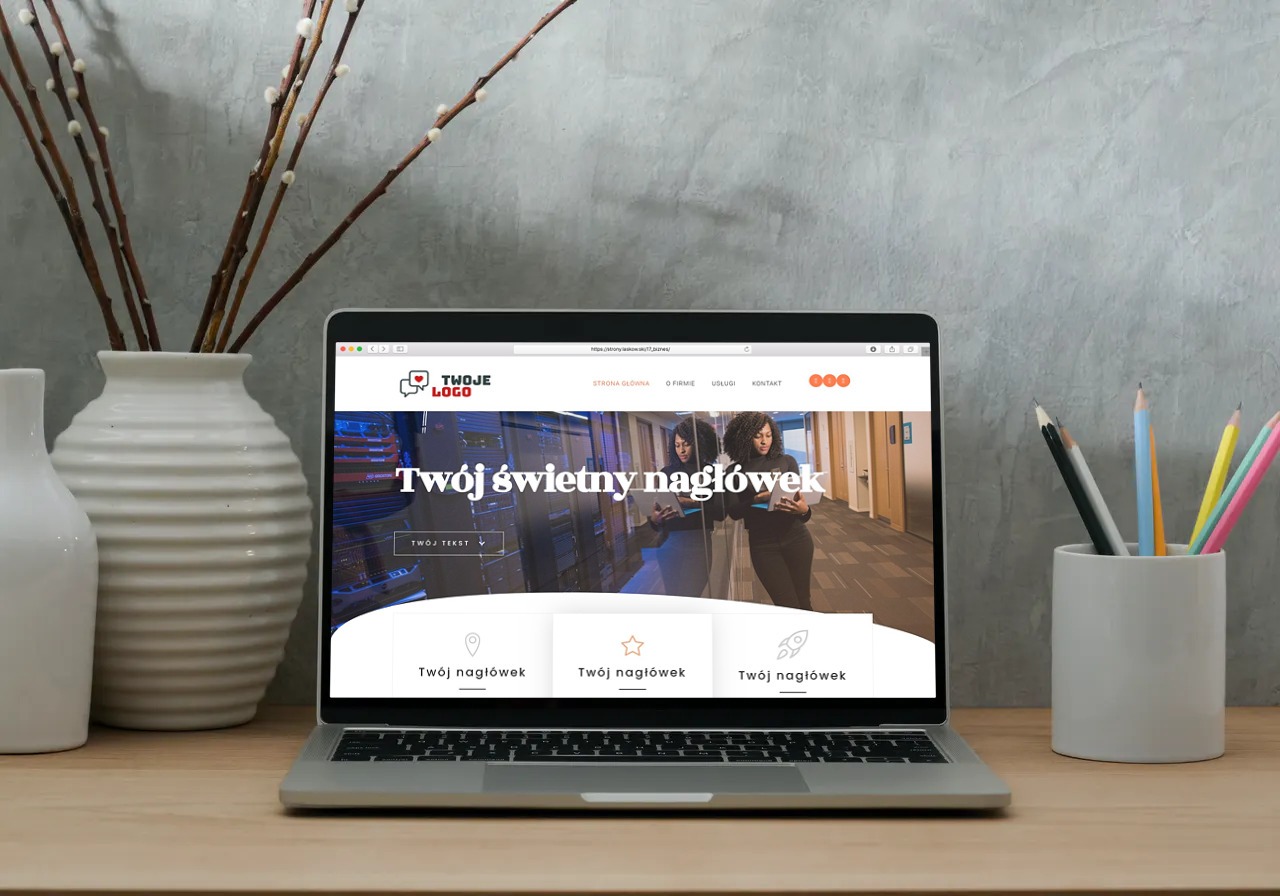 Laptop wyświetla przykładową stronę internetową z logo i nagłówkiem, obok w wazonie pędy wierzby i przybornik z kredkami na drewnianym biurku, szare tło.