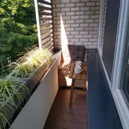 Przytulny balkon z białej cegły, drewnianą podłogą, drewnianymi lamelami, roślinami w donicach i małym stolikiem z dwoma filiżankami w słoneczny dzień.