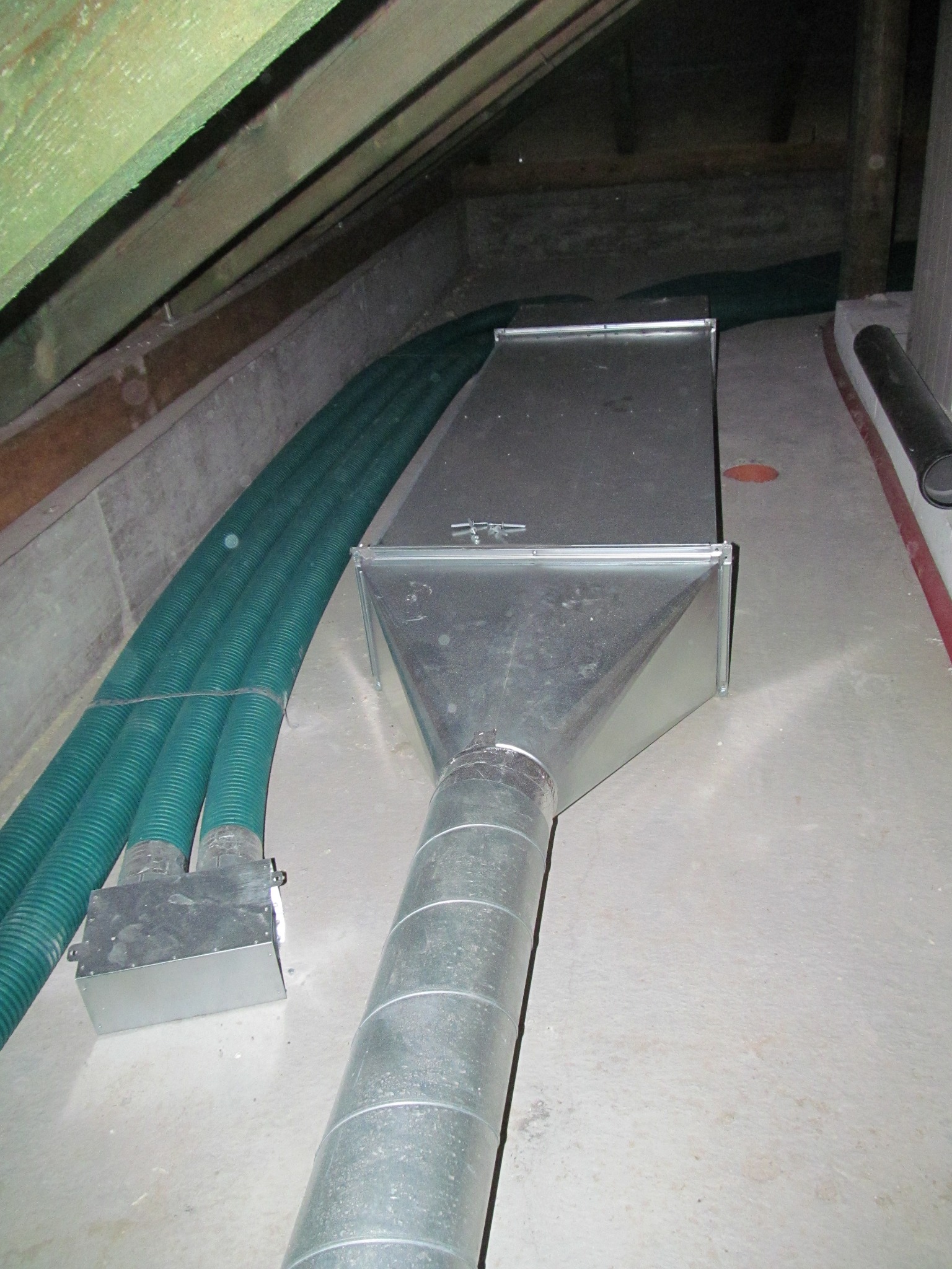 System wentylacyjny z ocynkowanej blachy w surowym pomieszczeniu, połączony z zielonymi rurami wentylacyjnymi.