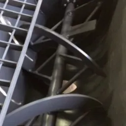 Wnętrze mieszalnika do betonu z widocznym pionowym wałem z przyspawanymi, spiralnymi łopatami, oraz górną kratą zabezpieczającą, wewnątrz stalowej konstrukcji.