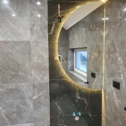 Wykończona łazienka z szarymi płytkami imitującymi marmur, okrągłe podświetlane lustro, nowoczesna lampa wisząca i okno z widokiem na schody.