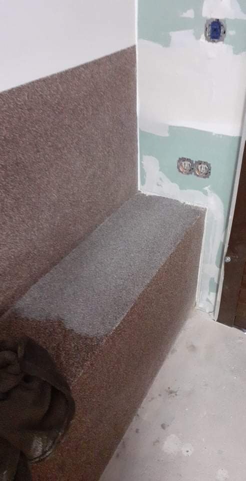 Ściana z nałożoną strukturą dekoracyjną w odcieniach brązu i szarości, widoczne puszki instalacyjne elektryczne w surowym stanie, ślady gładzi na ścianie