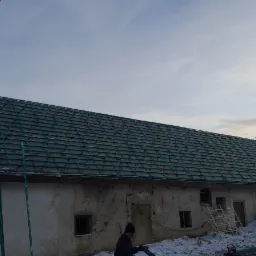 Montaż łat dachowych na budynku gospodarczym z widoczną drabiną i pracownikiem w zimowej scenerii.