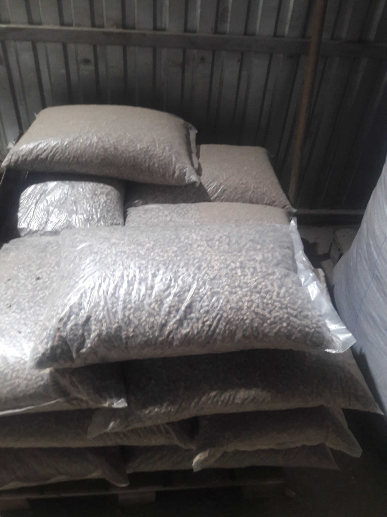 Stos worków z pelletem w magazynie o blaszanych ścianach, widoczne drobne nierówności na powierzchni worków.