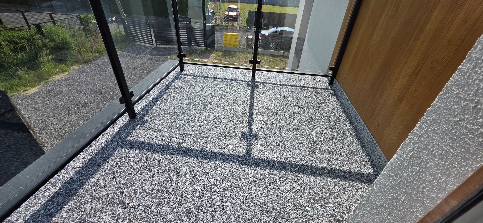 Szary taras z żywicy epoksydowej na balkonie z czarną balustradą i widokiem na zewnątrz. Widoczne detale wykończenia i faktura posadzki.