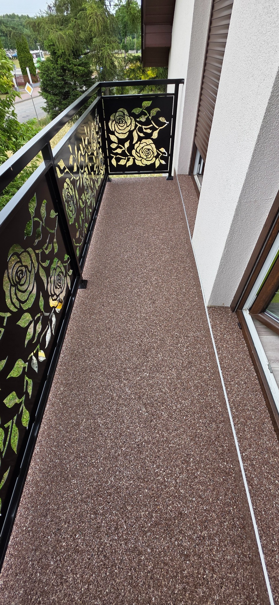 Balkon z posadzką żywiczną w odcieniach brązu i ozdobną balustradą z motywem róż, widok z góry.