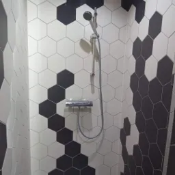 Kabina prysznicowa wyłożona heksagonalnymi płytkami w kolorze białym i czarnym, z zamontowaną baterią i słuchawką prysznicową.
