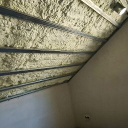 Gładzie i Malowanie Natryskowe - Poddasze z izolacją natryskową pianką PUR, widoczne metalowe profile pod płyty gipsowe. Na podłodze karton z armaturą łazienkową Grohe.