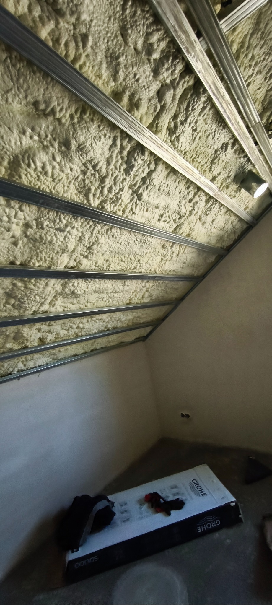 Poddasze z izolacją natryskową pianką PUR, widoczne metalowe profile pod płyty gipsowe. Na podłodze karton z armaturą łazienkową Grohe.