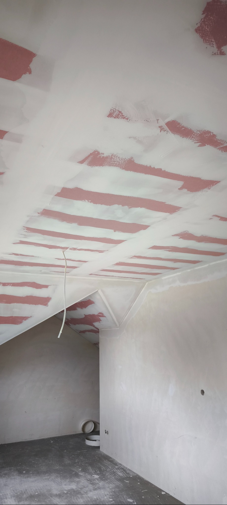 Pokój w trakcie remontu: częściowo zagruntowany sufit z widoczną instalacją elektryczną, ściany przygotowane do malowania. Na podłodze leżą taśmy malarskie.