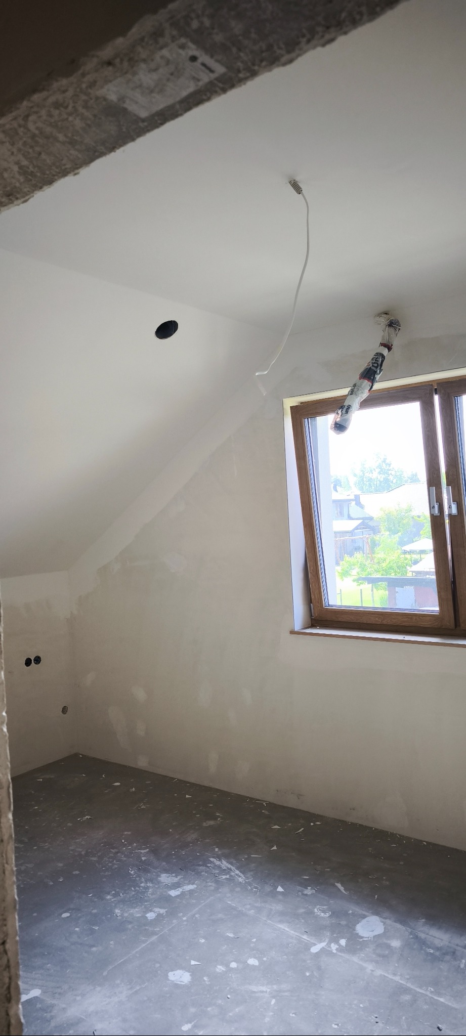 Poddasze po szpachlowaniu, ściany przygotowane pod malowanie. Widoczne okno i wystające kable. Na podłodze resztki gładzi.