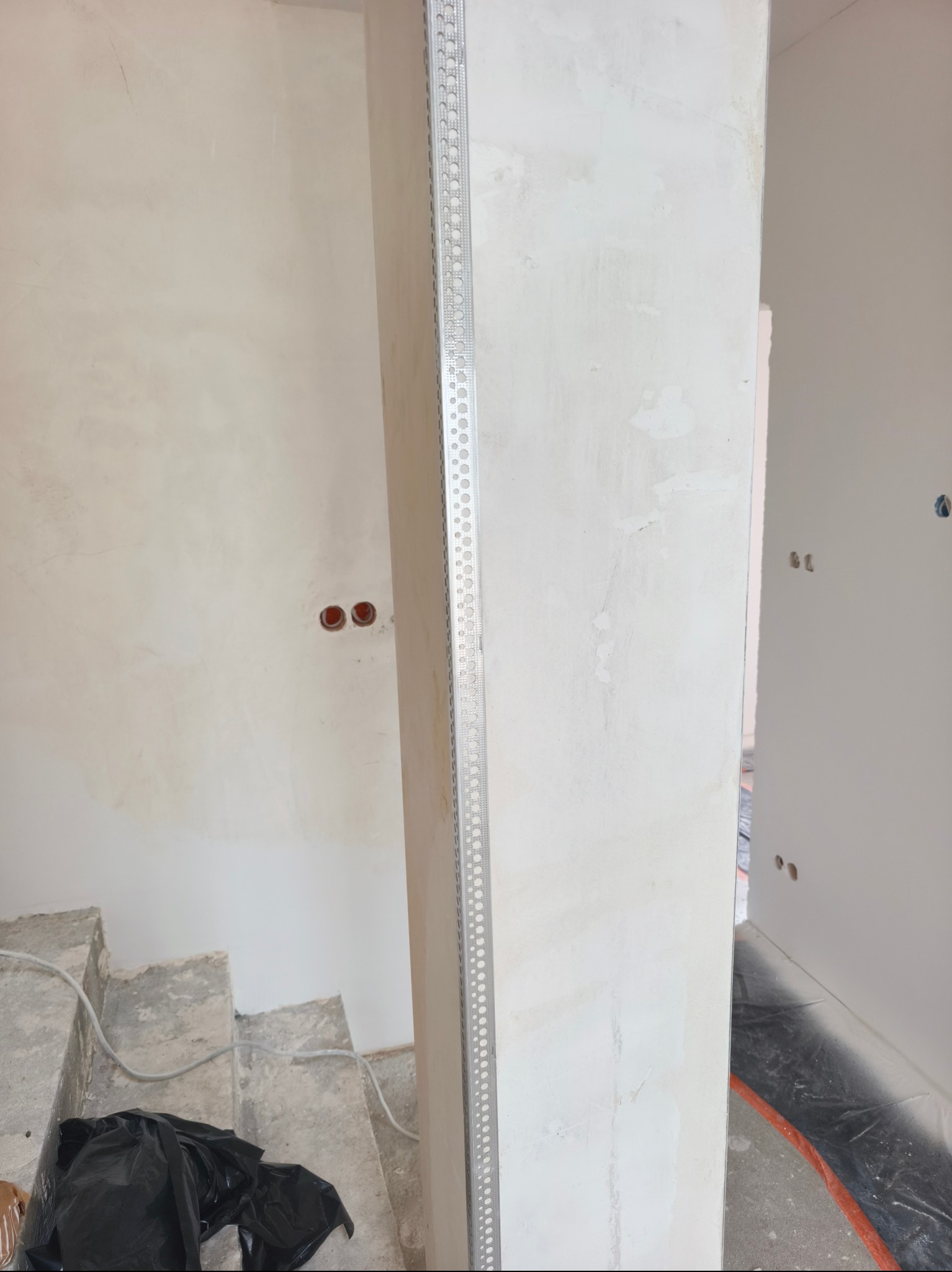 Ściana po szpachlowaniu, z narożnikiem aluminiowym i widocznymi śladami po gładzi, przygotowana do malowania w trakcie prac wykończeniowych.