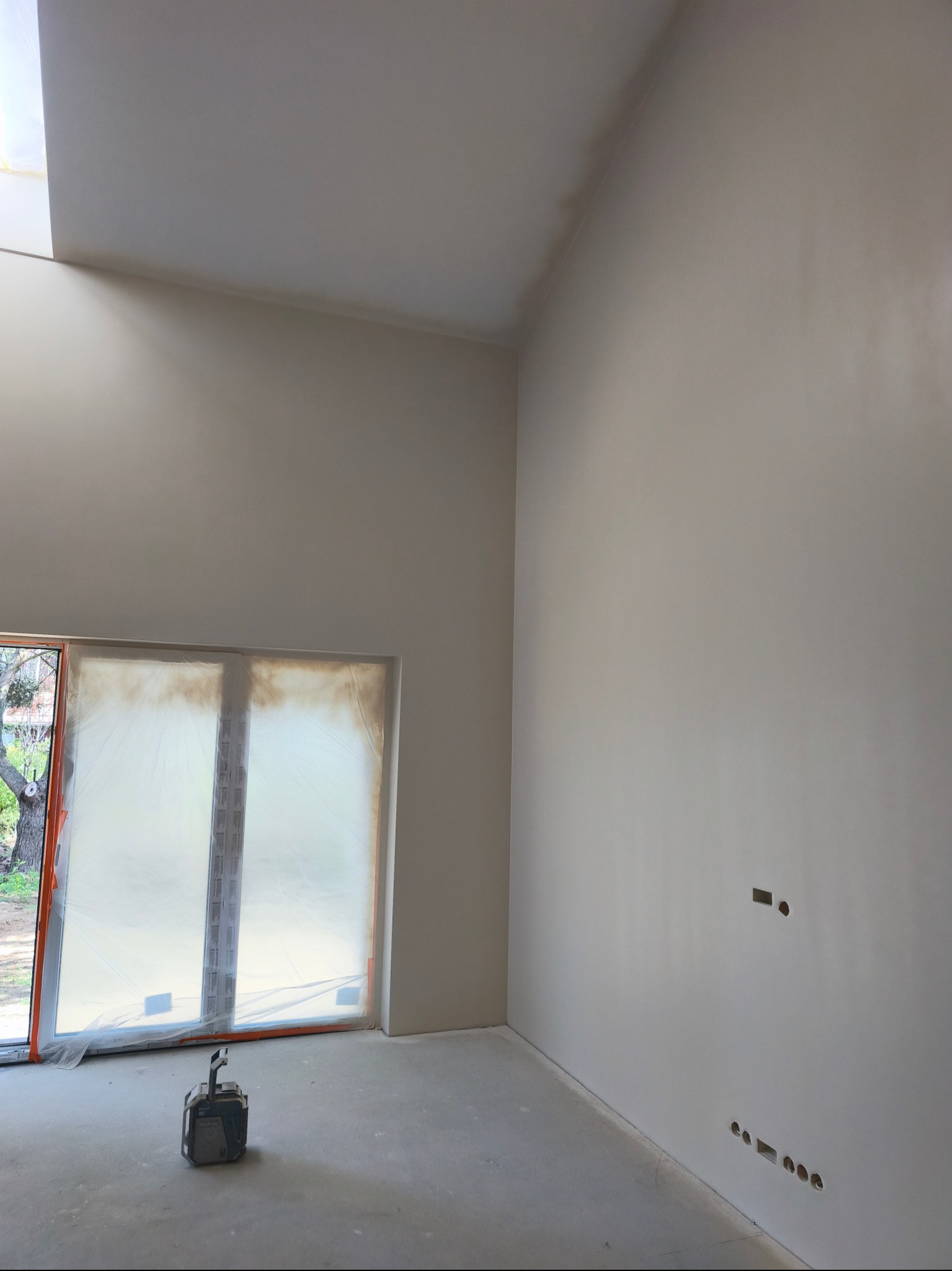 Wnętrze po gładziowaniu: gładkie, jasne ściany w nowym domu, okno zabezpieczone folią, szlifierka pod oknem, przygotowane punkty elektryczne na ścianie.